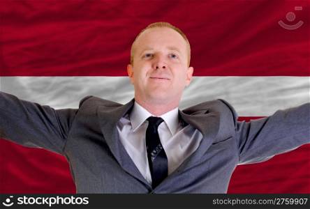 joyful investor spreading arms after good business investment in latvia, in front of flag