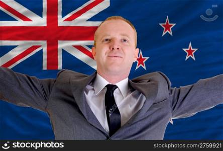 joyful investor spreading arms after good business investment in new zealand, in front of flag