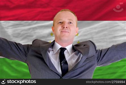 joyful investor spreading arms after good business investment in tajikistan, in front of flag