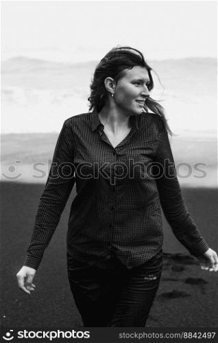 Joyful lady on black Iceland beach monochrome scenic photography. Picture of person with rough sea on background. High quality wallpaper. Photo concept for ads, travel blog, magazine, article. Joyful lady on black Iceland beach monochrome scenic photography