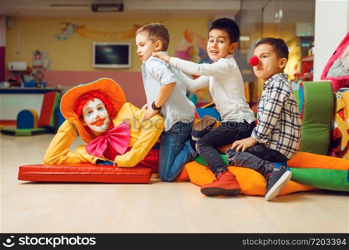 Joyful little boys sitting on funny clown in children&rsquo;s area. Birthday party celebrating in playroom, baby holiday in playground. Childhood happiness, childish leisure. Joyful little boys sitting on funny clown