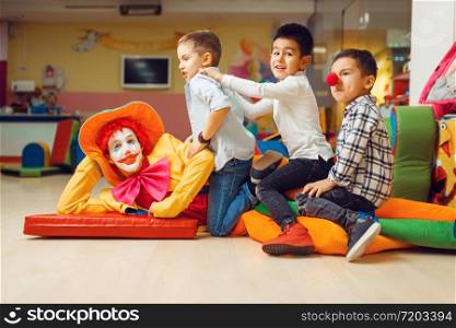 Joyful little boys sitting on funny clown in children&rsquo;s area. Birthday party celebrating in playroom, baby holiday in playground. Childhood happiness, childish leisure. Joyful little boys sitting on funny clown
