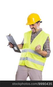 Joyful male engineer in yellow hardhat and reflective vest standing with clipboard on white background and celebrating success with clenched fist. Excited builder in uniform celebrating victory