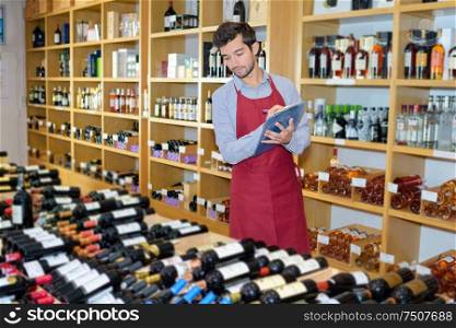 joyful male seller in uniform holding clipboard in wine shop