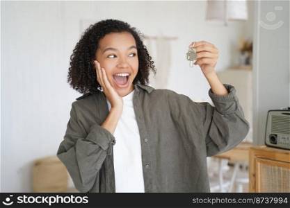 Joyful mixed race teen girl tenant showing keys to new home excited to move in, screaming wow. Happy young female renter buyer holding key, celebrates relocation to apartment. Rental service concept.. Happy mixed race girl showing keys to new home celebrates relocation to apartment. Rental service