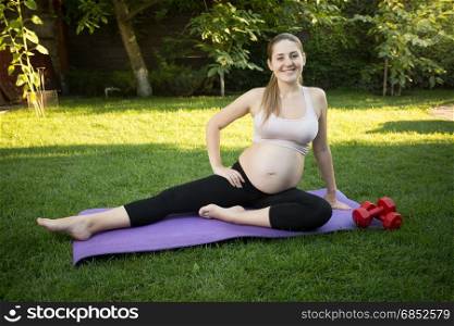 Joyful pregnant woman stretching on grass at park