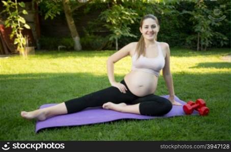 Joyful pregnant woman stretching on grass at park at sunny day