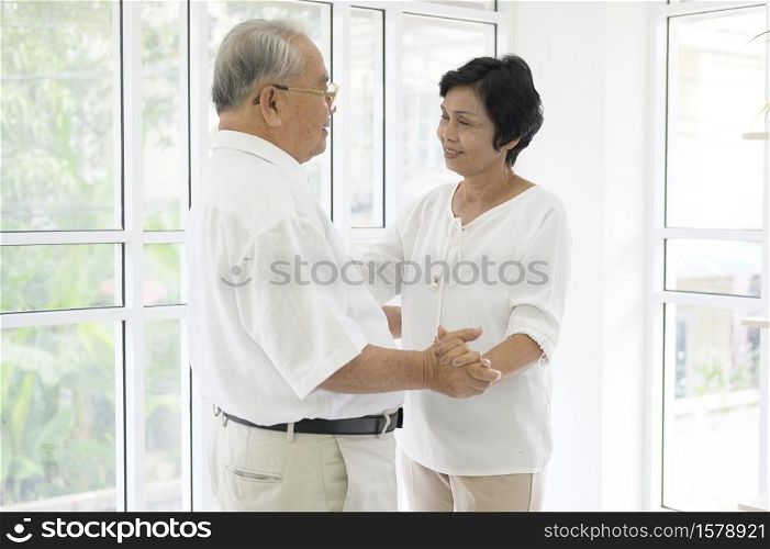 joyful senior asian retired couple is dancing and enjoying the music in the living room at home, health concept