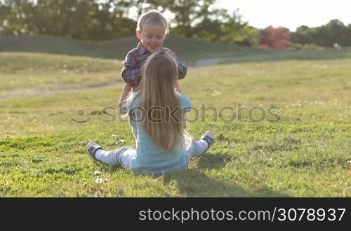 Joyful siblings playing and having fun together in green grassy field in park. Cute sister and her adorable toddler brother spending great time together while family relaxing outdoors.