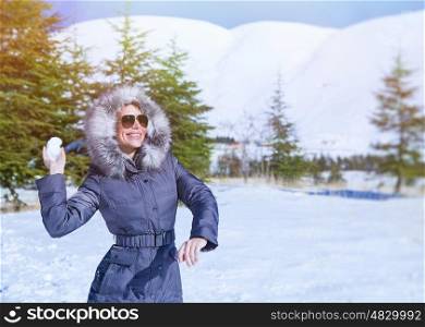 Joyful woman playing in the winter park, throwing snowballs, enjoying active wintertime game, having happy holidays&#xA;