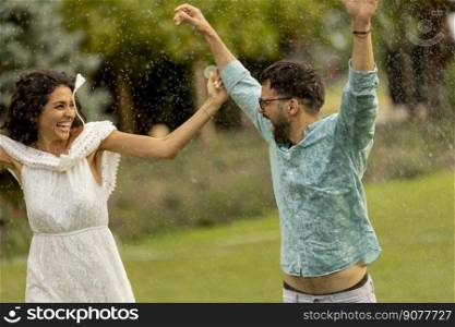 Joyful young couple caught by the sudden summer rain in the park
