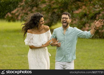 Joyful young couple caught by the sudden summer rain in the park