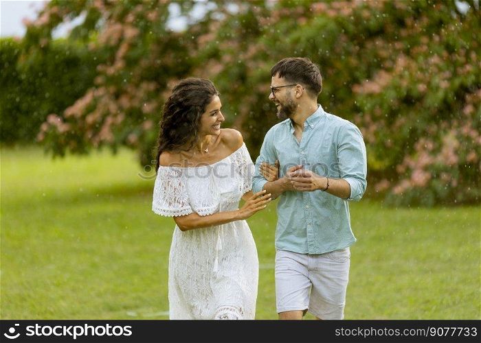 Joyful young couple caught by the sudden summer rain in the park
