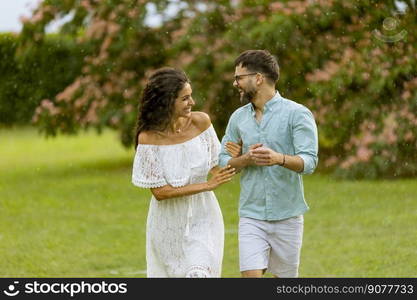 Joyful young couple caught by the sudden summer rain in the park