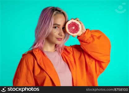Joyful young hipster woman with dyed pink hairstyle holding half of juicy grapefruit on eyes. Healthy lifestyle and eating concept. High quality photo. Joyful young hipster woman with dyed pink hairstyle holding half of juicy grapefruit on eyes. Healthy lifestyle and eating concept.
