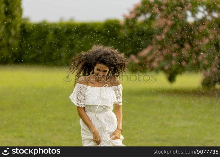 Joyful young woman caught by the sudden summer rain in the park