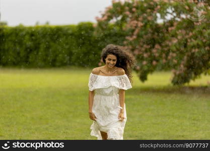 Joyful young woman caught by the sudden summer rain in the park