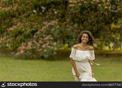 Joyful young woman caught by the sudden summer rain in the park