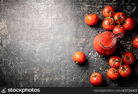 Jug with tomato juice on the table. On a black background. High quality photo. Jug with tomato juice on the table.