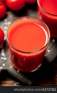 Juice from ripe tomatoes in a glass. On a wooden background. High quality photo. Juice from ripe tomatoes in a glass.