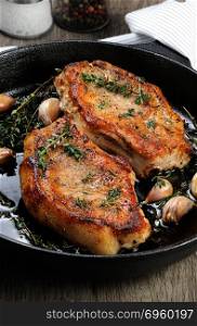 Juicy, browned pork steak on a bone in oil with garlic and herbs in a frying pan.. Roasted pork steak in frying pan