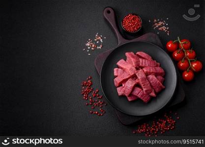 Juicy fresh raw beef meat with salt, spices and herbs on a dark textured concrete background