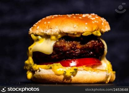 Juicy grilled beef cheeseburger isolated on black background. Cheeseburger with melted cheese on black stone plate.