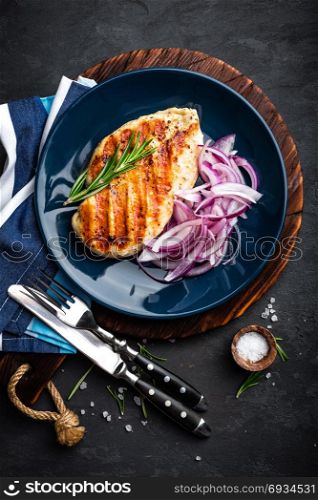 Juicy grilled chicken meat, fillet with fresh marinated onion on plate. Black background, top view