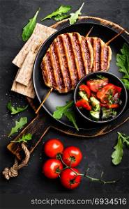 Juicy grilled chicken meat lula kebab on skewers with fresh vegetable salad on black background, top view