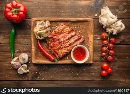 Juicy grilled ribs and piece of meat on wooden table, top view nobody. Pepper, garlic and herb on background