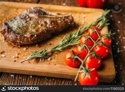 Juicy grilled steak on the bone and tomatoes on a branch closeup, nobody. Meat dish on wooden table