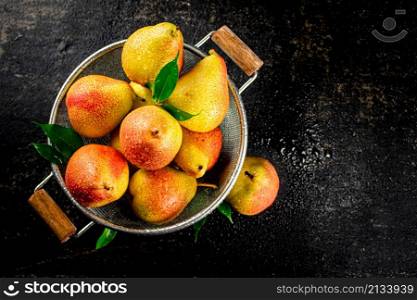 Juicy pears in a colander with foliage. On a black background. High quality photo. Juicy pears in a colander with foliage.