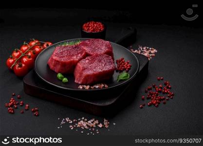 Juicy raw beef with spices, salt and herbs on a dark concrete background. Preparing to cook a meat dish. Juicy raw beef with spices, salt and herbs on a dark concrete background