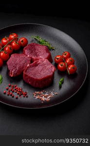 Juicy raw beef with spices, salt and herbs on a dark concrete background. Preparing to cook a meat dish. Juicy raw beef with spices, salt and herbs on a dark concrete background