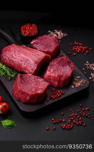 Juicy raw beef with spices, salt and herbs on a dark concrete background. Preparing to cook a meat dish. Juicy raw beef with spices, salt and herbs on a dark concrete background