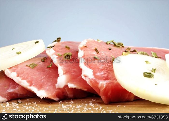 Juicy raw pork loin chops with onion slices and spices on wooden cutting board with copy space.