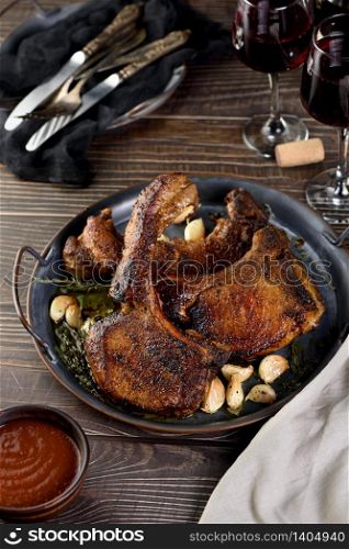Juicy, slice of fried pork chop on a bone in oil with garlic and herbs in a pan.