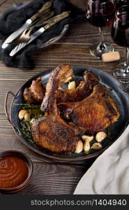 Juicy, slice of fried pork chop on a bone in oil with garlic and herbs in a pan.