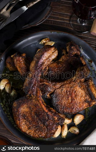 Juicy, slice of fried pork chop on a bone in oil with garlic and herbs in a pan. Flat lay