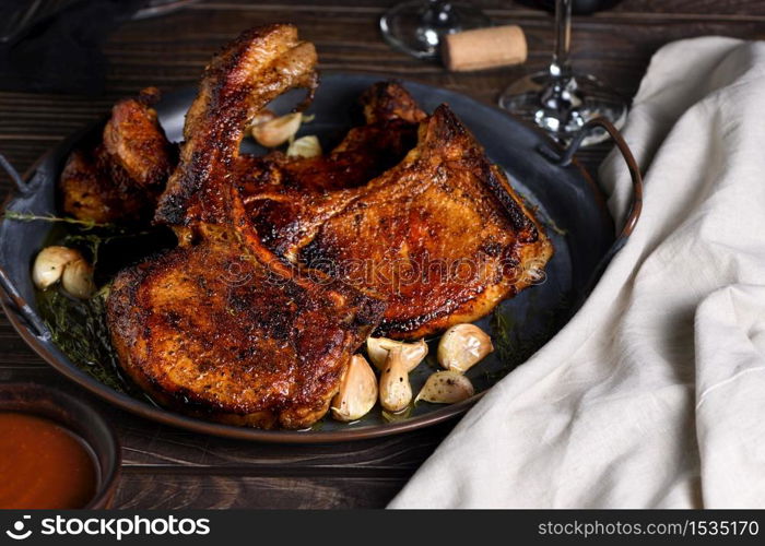 Juicy, slice of fried pork chop on a bone in oil with garlic and herbs in a pan. Close-up.