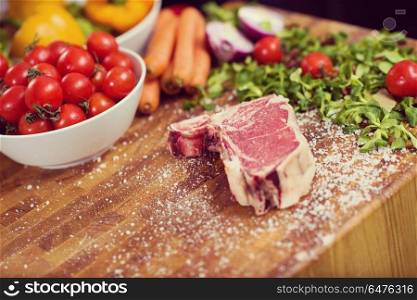 Juicy slice of raw steak with vegetables around on a wooden table. Juicy slice of raw steak on wooden table