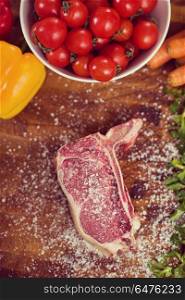 Juicy slice of raw steak with vegetables around on a wooden table top view. top view of raw steak on wooden table