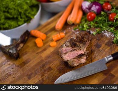 Juicy slices of grilled steak with vegetables around on a wooden board. Juicy slices of grilled steak on wooden board
