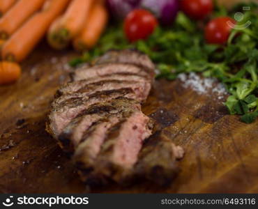 Juicy slices of grilled steak with vegetables around on a wooden board. Juicy slices of grilled steak on wooden board