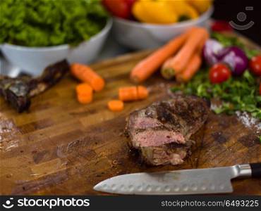 Juicy slices of grilled steak with vegetables around on a wooden board. Juicy slices of grilled steak on wooden board