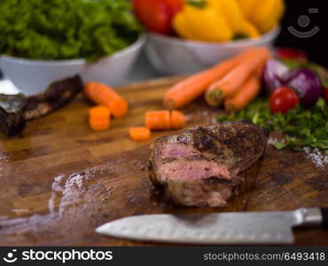 Juicy slices of grilled steak with vegetables around on a wooden board. Juicy slices of grilled steak on wooden board