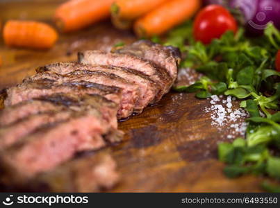 Juicy slices of grilled steak with vegetables around on a wooden board. Juicy slices of grilled steak on wooden board