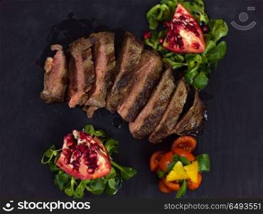 Juicy slices of grilled steak with vegetables on a wooden board, top view. Juicy slices of grilled steak
