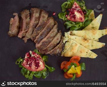Juicy slices of grilled steak with vegetables on a wooden board, top view. Juicy slices of grilled steak