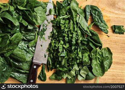 Juicy spinach leaves chopped on a wooden cutting board. The chef?s knife lies on the table, top view. Organic and healthy food. The idea of making breakfast